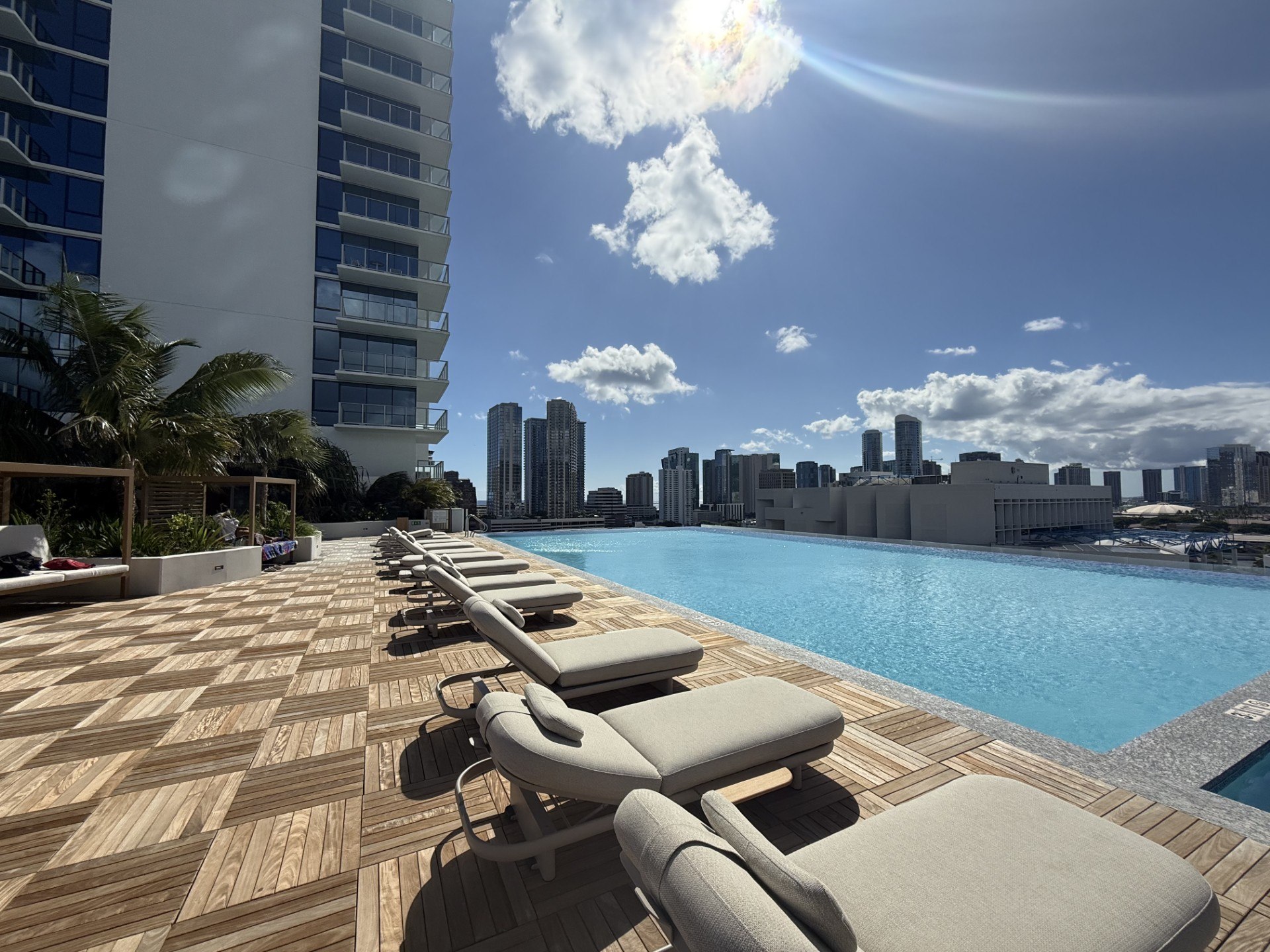 A row of sun loungers are on a wooden deck next to a swimming pool.
